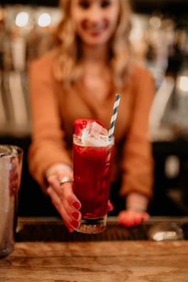 A close-up of a vibrant cocktail being handed over with a smile at a lively house party