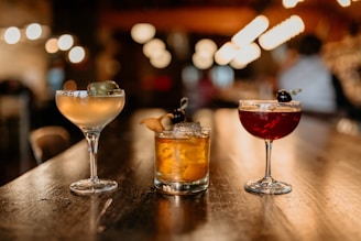 two glasses of different types of drinks on a bar