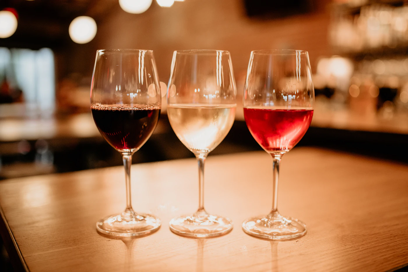 Drie proefglazen naast elkaar op een tafel met rode wijn, witte wijn en rose