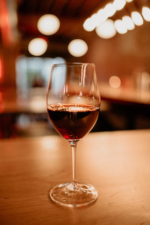 Close-up of a rustic wooden table with a bottle of aged red wine and two glasses glowing softly in warm light.