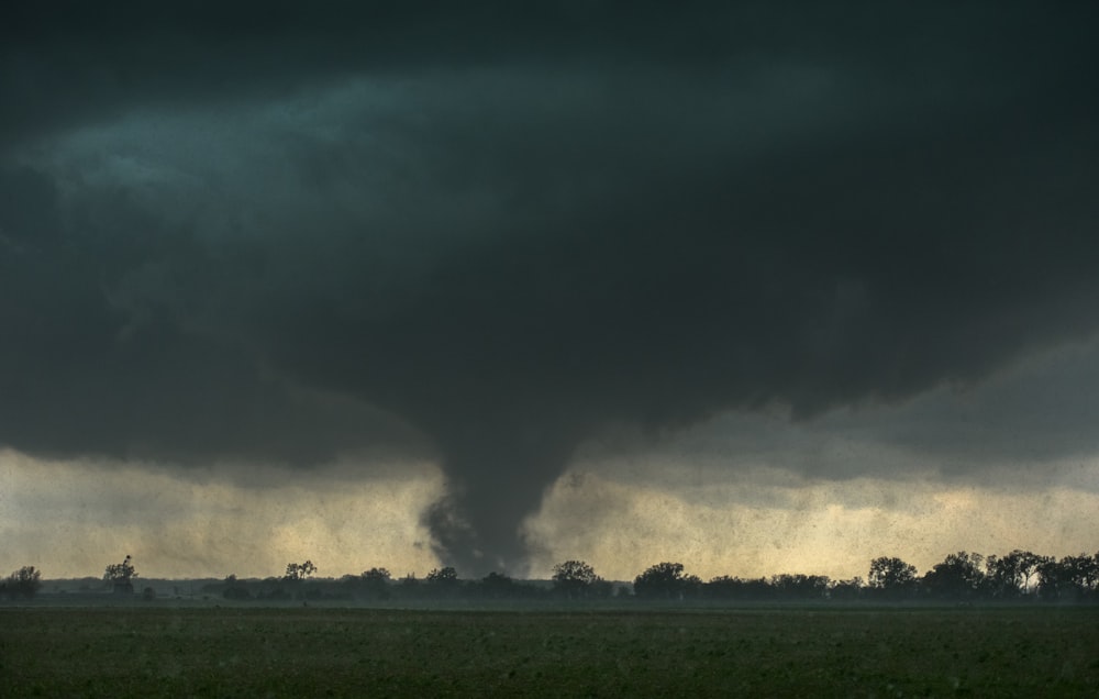 a large black cloud is in the sky over a field