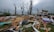 A scene of destruction and debris with splintered wood, scattered belongings, and damaged trees. The remnants of a structure, possibly a house, are partially visible amidst the wreckage. The sky is overcast, contributing to the somber atmosphere.