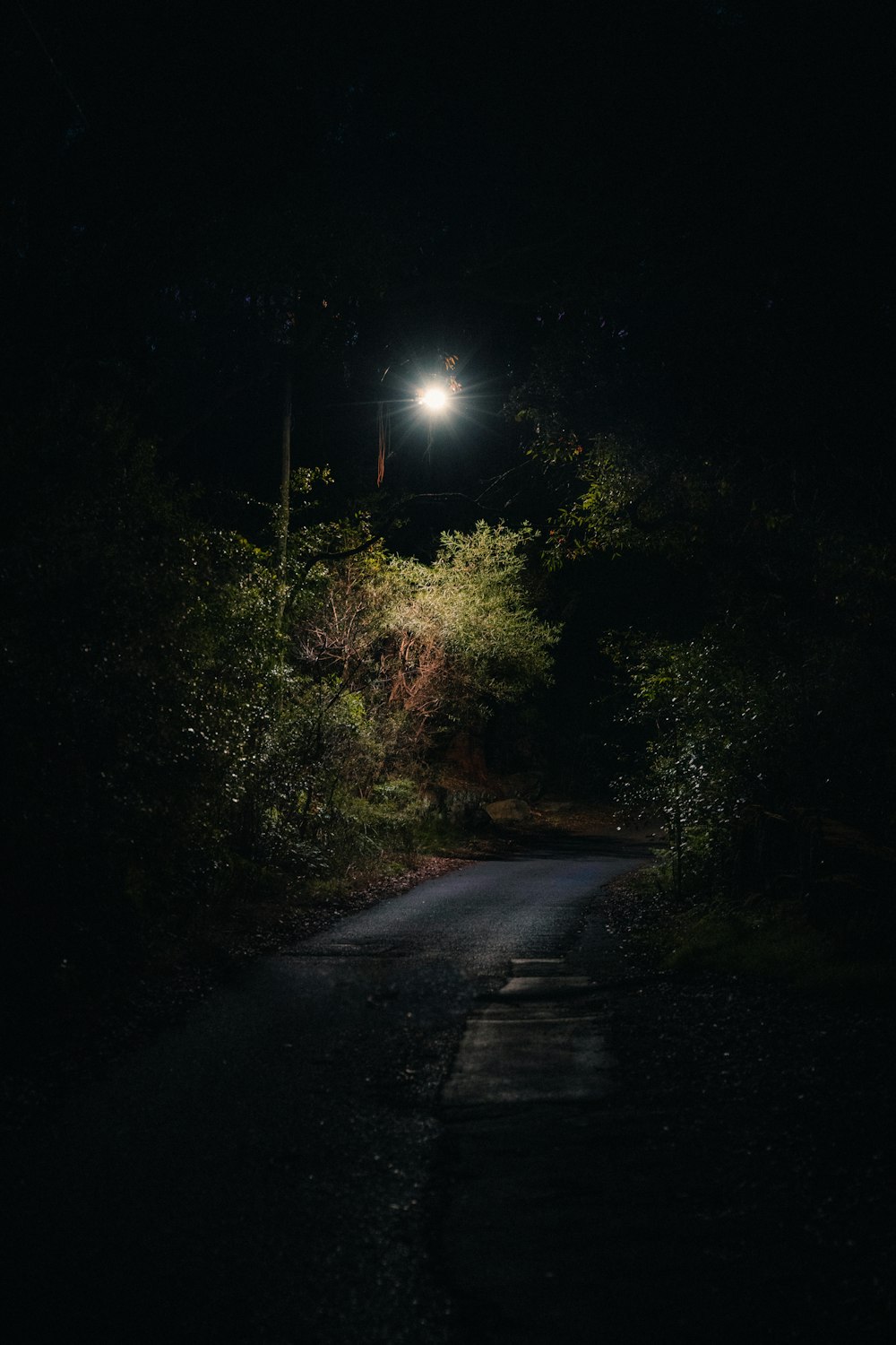 a dark road at night with a street light in the distance
