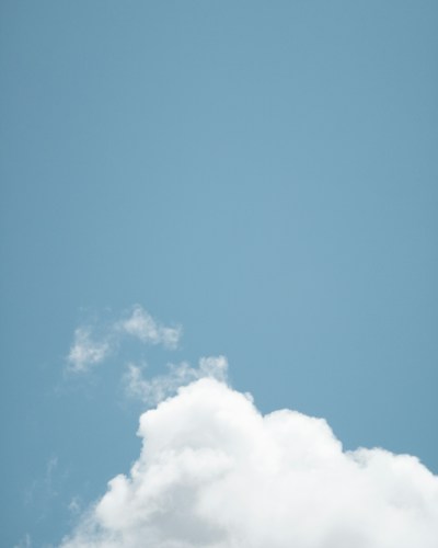 A clear blue sky with a single, large white fluffy cloud taking up most of the lower part of the image. The sky is mostly empty, creating a sense of openness and tranquility.