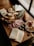 A wooden board displays an assortment of sliced breads, cheese triangles, green beans, cured meats, olives, and a bread roll. The arrangement is artful and appears to be prepared for a charcuterie presentation.