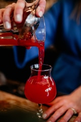 A close-up of a hand pouring a vibrant elixir into a glass, symbolizing refined rewards.