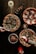 A wooden table is adorned with three different pizzas. One pizza has fresh greens and prosciutto, another is topped with pepperoni and charred vegetables, and the third features mushrooms with a drizzle of sauce. On the table, there is also a salad with colorful vegetables and two hands reaching in to serve themselves. Small stuffed mushrooms are arranged on a rectangular plate. Candles provide warm ambient lighting, and there are glasses of cocktails and red drinks accompanied by citrus garnishes.