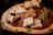 A wooden platter with an assortment of gourmet foods. There are several varieties of cheese, with one piece topped with some blackberries and drizzled with a dark syrup. Additionally, there are green beans laid out alongside honeycomb and toasted bread slices.
