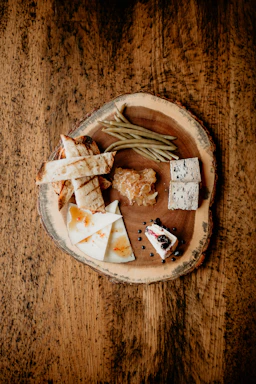A rustic wooden board displaying a colorful assortment of fresh food items from the menu, including tartines and salads, in a cozy bar setting.