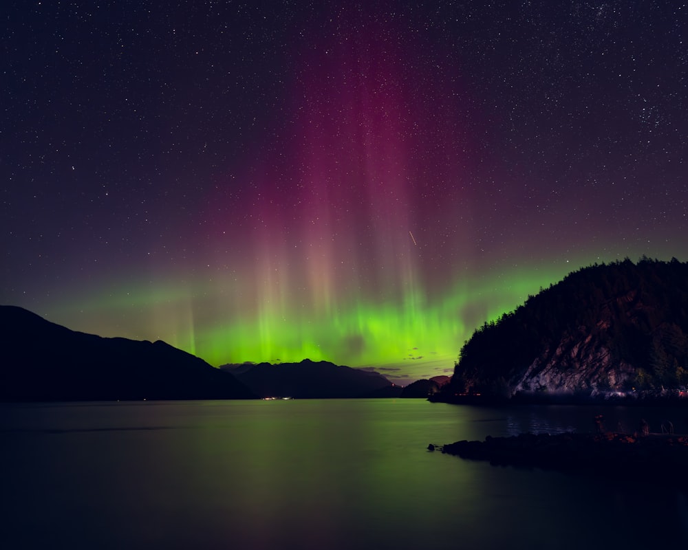 a green and purple aurora bore over a body of water