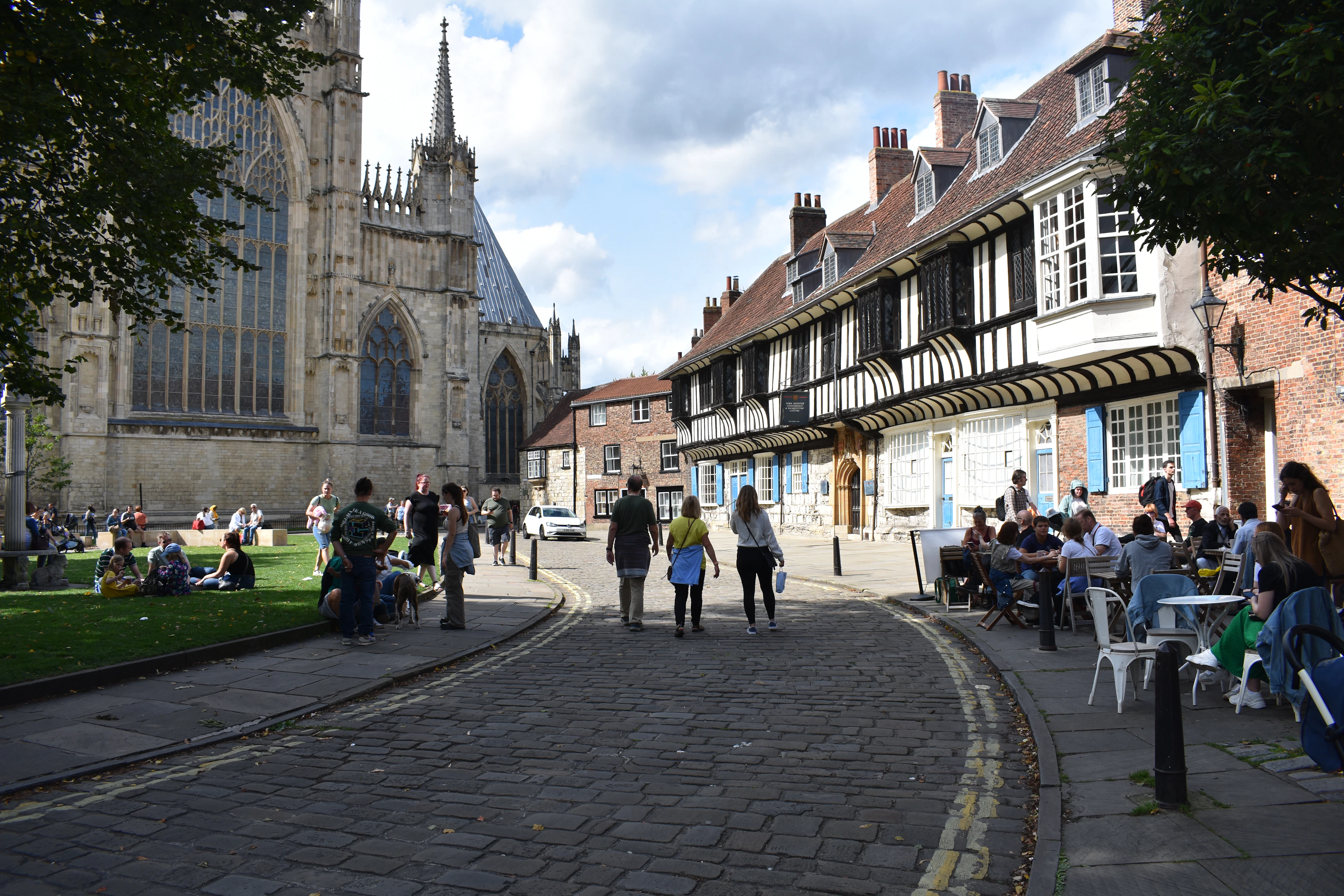 A cobbled street beside York Minster, timbered buildings and cafe tables along one side