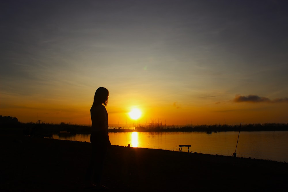a person standing in front of a body of water at sunset