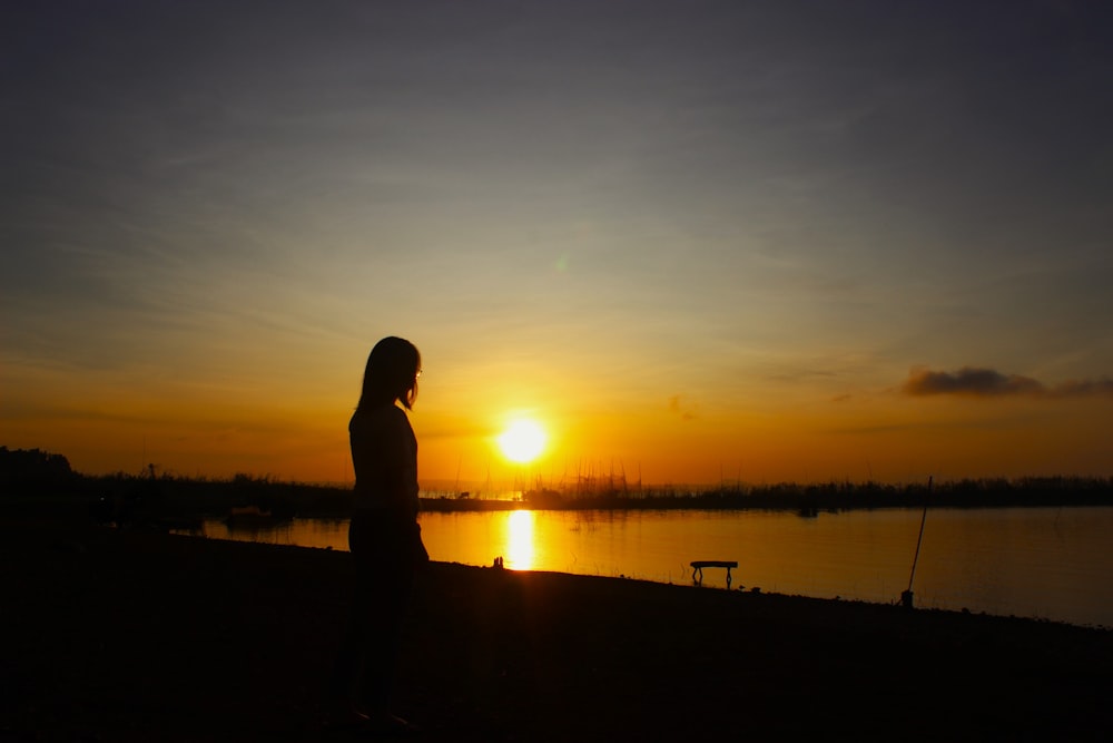 uma pessoa em pé na frente de um corpo de água ao pôr do sol