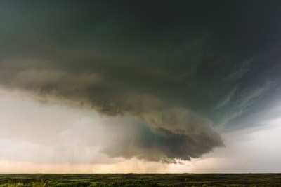 A massive storm cloud dominates the sky, swirling with dense, dark formations over an open, grassy plain. The cloud appears heavy with rain, and the atmosphere is charged with the impending sense of a storm.