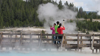 A warm, inviting photo of a small group on a guided tour near Old Faithful geyser with lush forest backdrop.