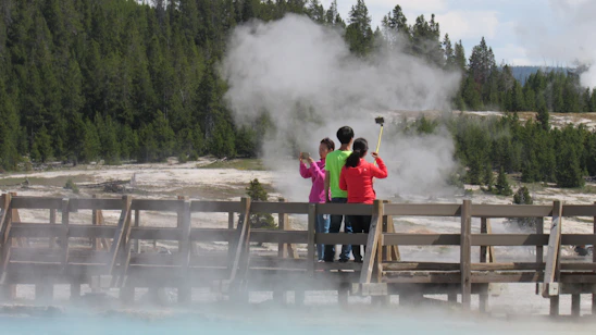 A warm, inviting photo of a small group on a guided tour near Old Faithful geyser with lush forest backdrop.