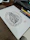 A laptop screen displaying elegant Arabic calligraphy templates surrounded by design sketches and coffee.