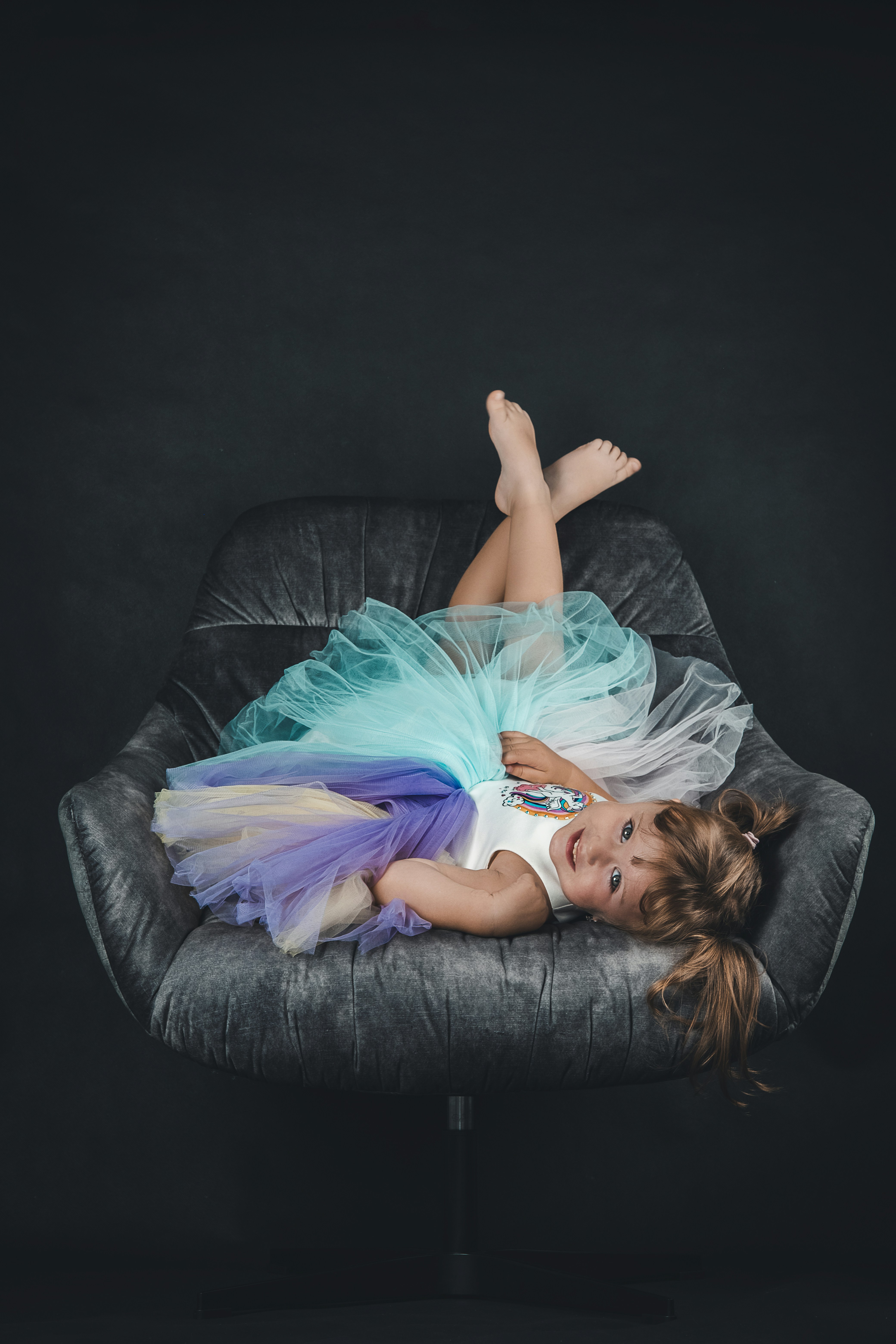 a little girl in a dress laying on a chair