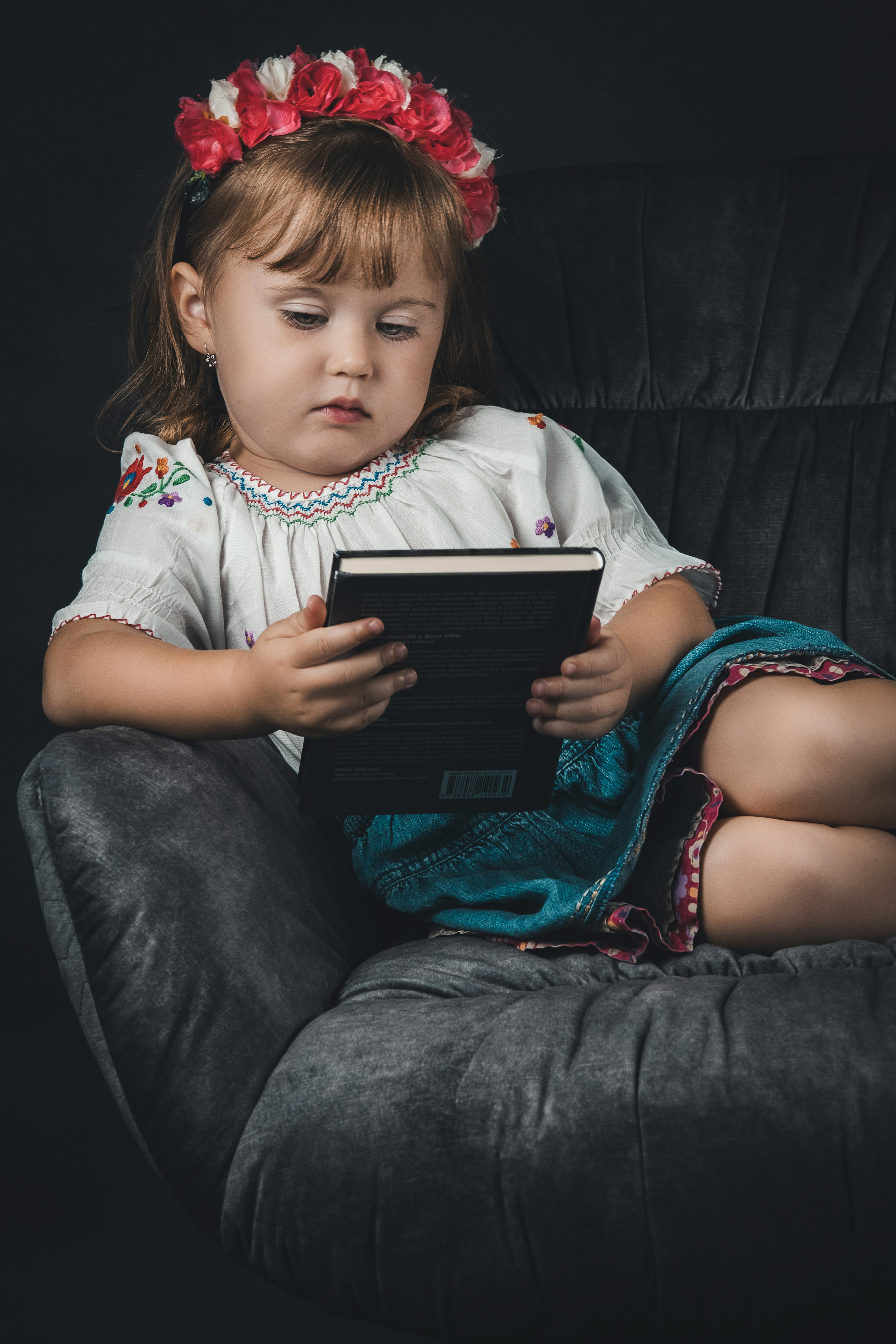 a little girl sitting in a chair reading a book