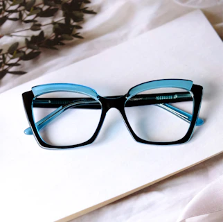 A pair of elegant black frames with subtle gold accents placed beside a vintage book.