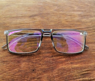 Close-up of eyeglasses with clear, reflective lenses on a wooden table.