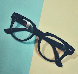 A stylish pair of black and gold eyeglasses on a beige background.