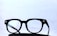 Black-framed eyeglasses placed on a dark surface with a light, minimalistic background. The glasses have a classic design with clear lenses.