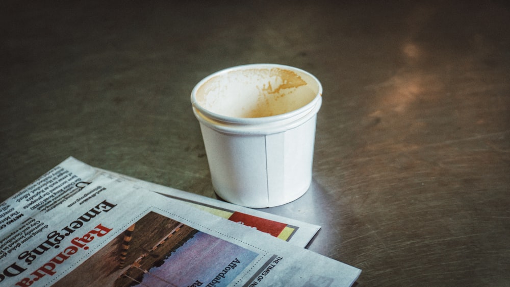 a cup of coffee sitting on top of a table next to a newspaper