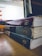 A stack of three worn textbooks with visible spines, labeled with different subjects, sits on a wooden table beside a glowing laptop screen displaying a website. The focus is on the books, with their aged and rough edges noticeable.