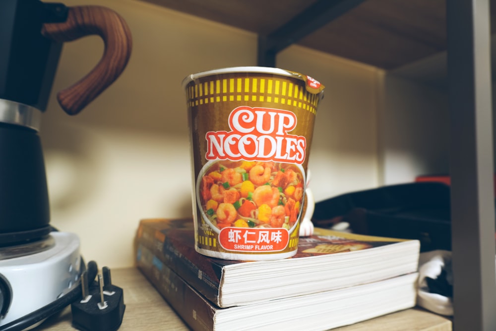 a cup of noodles sitting on top of a stack of books