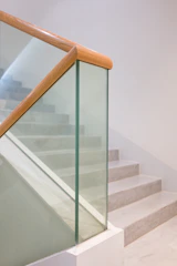 Jasne schody ze szklaną balustradą i drewnianą poręczą.