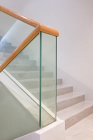 Jasne schody ze szklaną balustradą i drewnianą poręczą.