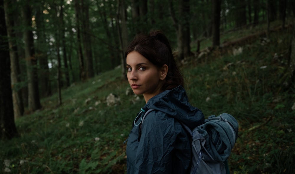 a woman in a blue jacket is standing in the woods