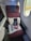 A first-class airplane seat with a maroon fabric upholstery is adjacent to two airplane windows. On the seat, a white pillow, a blanket in clear packaging, a pair of slippers, an amenity kit labeled with 'Japan Airlines', and a small red bag are neatly arranged.