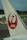 A close-up view of an airplane tail featuring a red logo of a stylized crane and the letters 'JAL' against a white background. The background includes airport tarmac, equipment, and distant trees under a cloudy sky.
