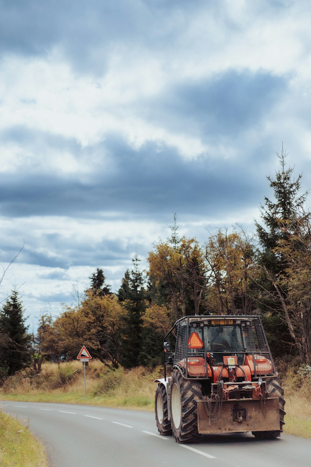 a tractor driving down a road with trees in the background