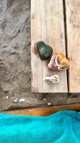 Several uniquely shaped stones rest on a wooden surface, with a sandy texture visible in the background. A vibrant turquoise fabric is seen at the lower edge, adding contrast to the natural colors of the stones and wood.
