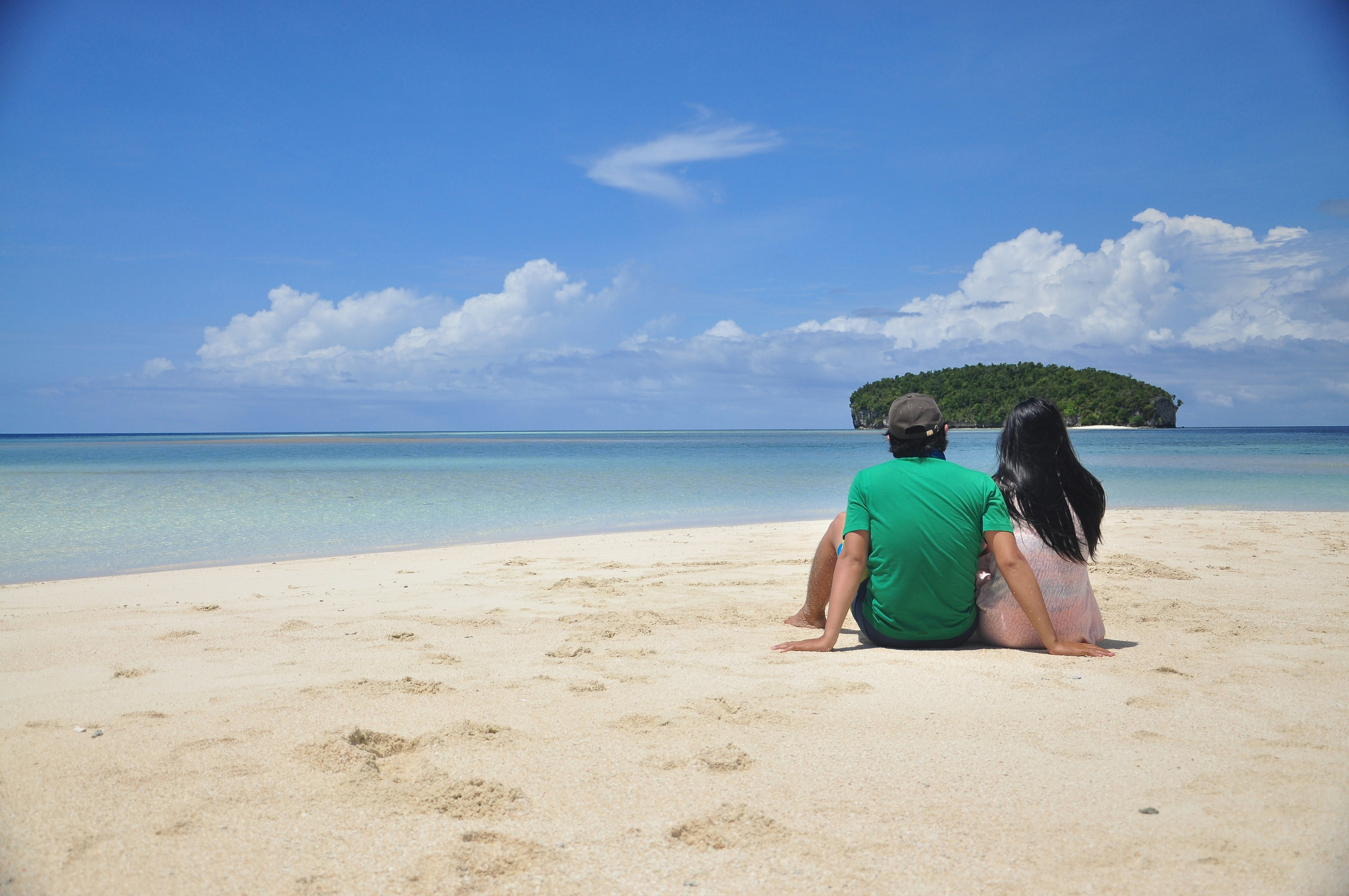 two people sitting on a beach looking out at the ocean