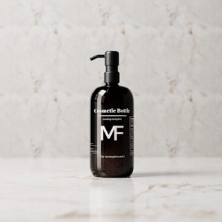 A sleek, black cosmetic bottle with a pump is placed on a light marble surface. The bottle features bold white text and branding, standing out against the reflective dark surface.