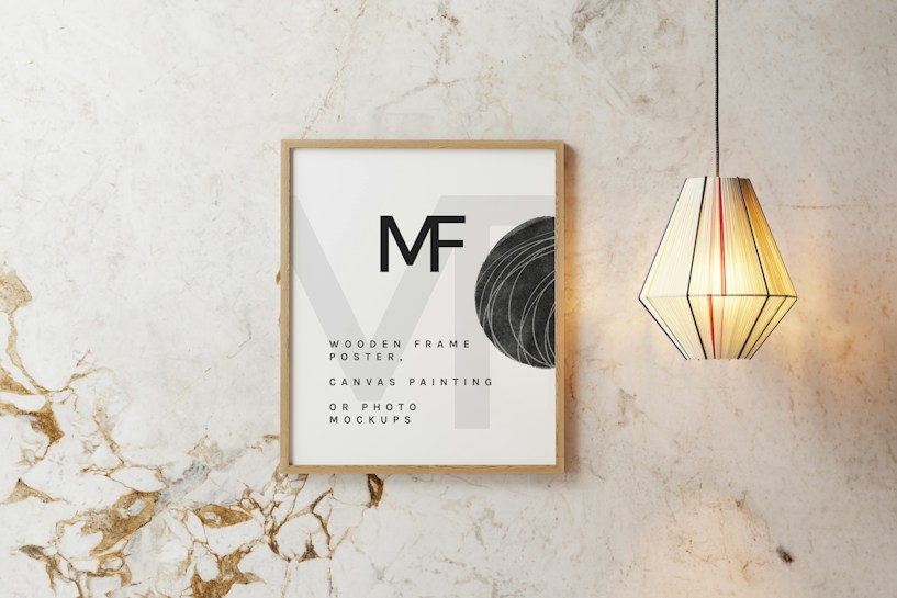 A wooden frame with minimalist text and design elements is displayed on a marble-textured wall. Next to the frame, a geometric pendant light with vertical stripes emits a warm glow.