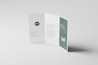 A clean and minimalist tri-fold brochure displayed on a light gray surface. The brochure is partially open, revealing sections with text and graphical elements. A prominent &lsquo;MF&rsquo; logo appears, and there are styled text blocks.