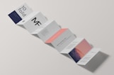A minimalist design of a folded brochure mockup is displayed against a light background. The sequence of panels shows varied typography and graphics, with a mix of dark blue, white, and peach colors. Some panels contain textual content, while one has an abstract image resembling a mountain with a gradient sky.