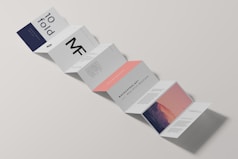 A minimalist design of a folded brochure mockup is displayed against a light background. The sequence of panels shows varied typography and graphics, with a mix of dark blue, white, and peach colors. Some panels contain textual content, while one has an abstract image resembling a mountain with a gradient sky.