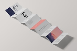 A minimalist design of a folded brochure mockup is displayed against a light background. The sequence of panels shows varied typography and graphics, with a mix of dark blue, white, and peach colors. Some panels contain textual content, while one has an abstract image resembling a mountain with a gradient sky.