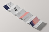 A minimalist design of a folded brochure mockup is displayed against a light background. The sequence of panels shows varied typography and graphics, with a mix of dark blue, white, and peach colors. Some panels contain textual content, while one has an abstract image resembling a mountain with a gradient sky.