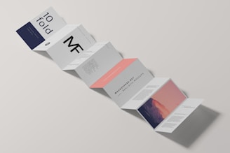 A minimalist design of a folded brochure mockup is displayed against a light background. The sequence of panels shows varied typography and graphics, with a mix of dark blue, white, and peach colors. Some panels contain textual content, while one has an abstract image resembling a mountain with a gradient sky.