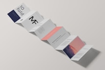 A minimalist design of a folded brochure mockup is displayed against a light background. The sequence of panels shows varied typography and graphics, with a mix of dark blue, white, and peach colors. Some panels contain textual content, while one has an abstract image resembling a mountain with a gradient sky.