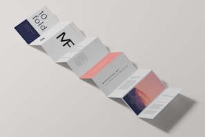 A minimalist design of a folded brochure mockup is displayed against a light background. The sequence of panels shows varied typography and graphics, with a mix of dark blue, white, and peach colors. Some panels contain textual content, while one has an abstract image resembling a mountain with a gradient sky.