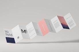A series of connected rectangular paper flaps arranged in a zigzag pattern, featuring text and imagery. The paper design includes various sections with different colors such as white, navy, pink, and a section with a mountain landscape image. The layout appears professional and modern, with clean typography and minimalistic design elements.