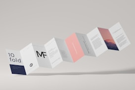 A series of connected rectangular paper flaps arranged in a zigzag pattern, featuring text and imagery. The paper design includes various sections with different colors such as white, navy, pink, and a section with a mountain landscape image. The layout appears professional and modern, with clean typography and minimalistic design elements.